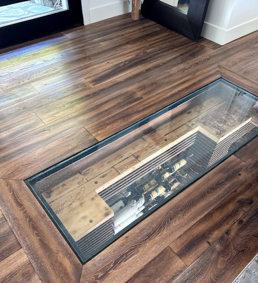 Wooden floor with glass floor topped wine cellar, showing bottles in a recessed space.