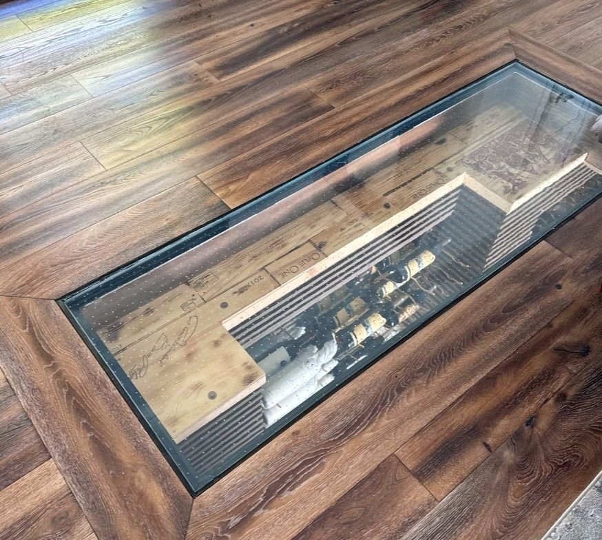 Glass floor wine cellar in a wooden floor. Bottles visible below the glass.
