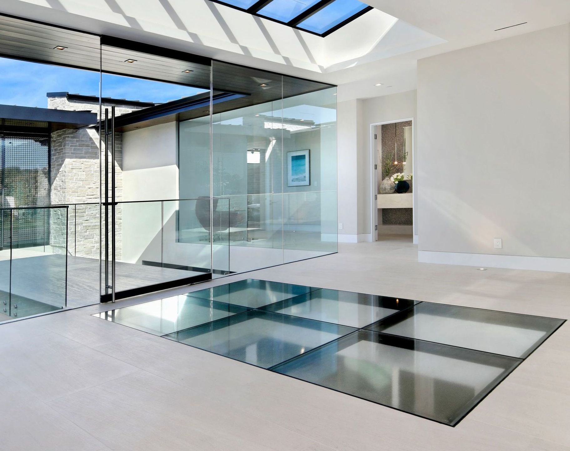 Spacious modern interior with glass floor panels, large windows, and a light-filled open design.
