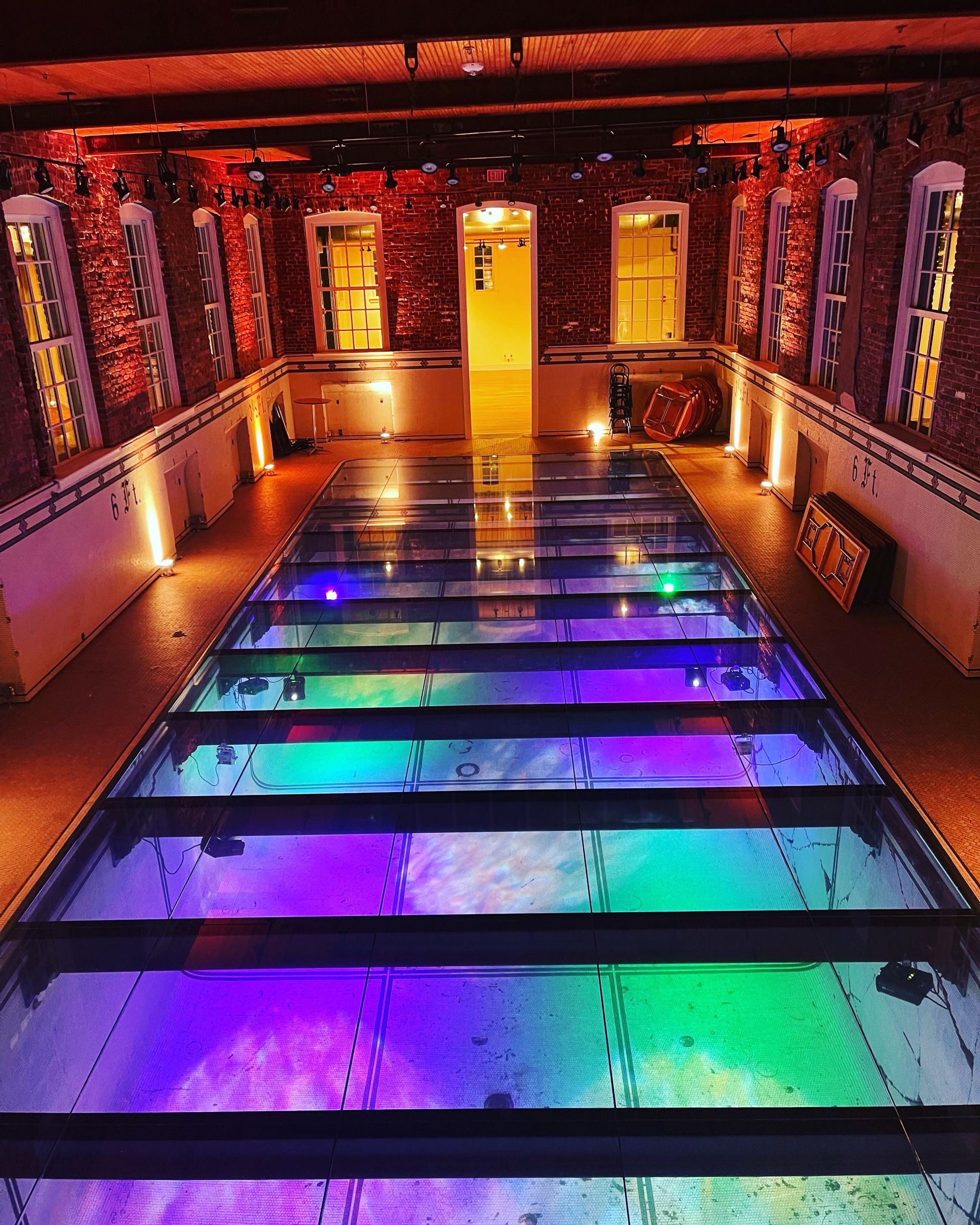 Custom glass flooring illuminated with multicolor LED lights over a historical swimming pool.