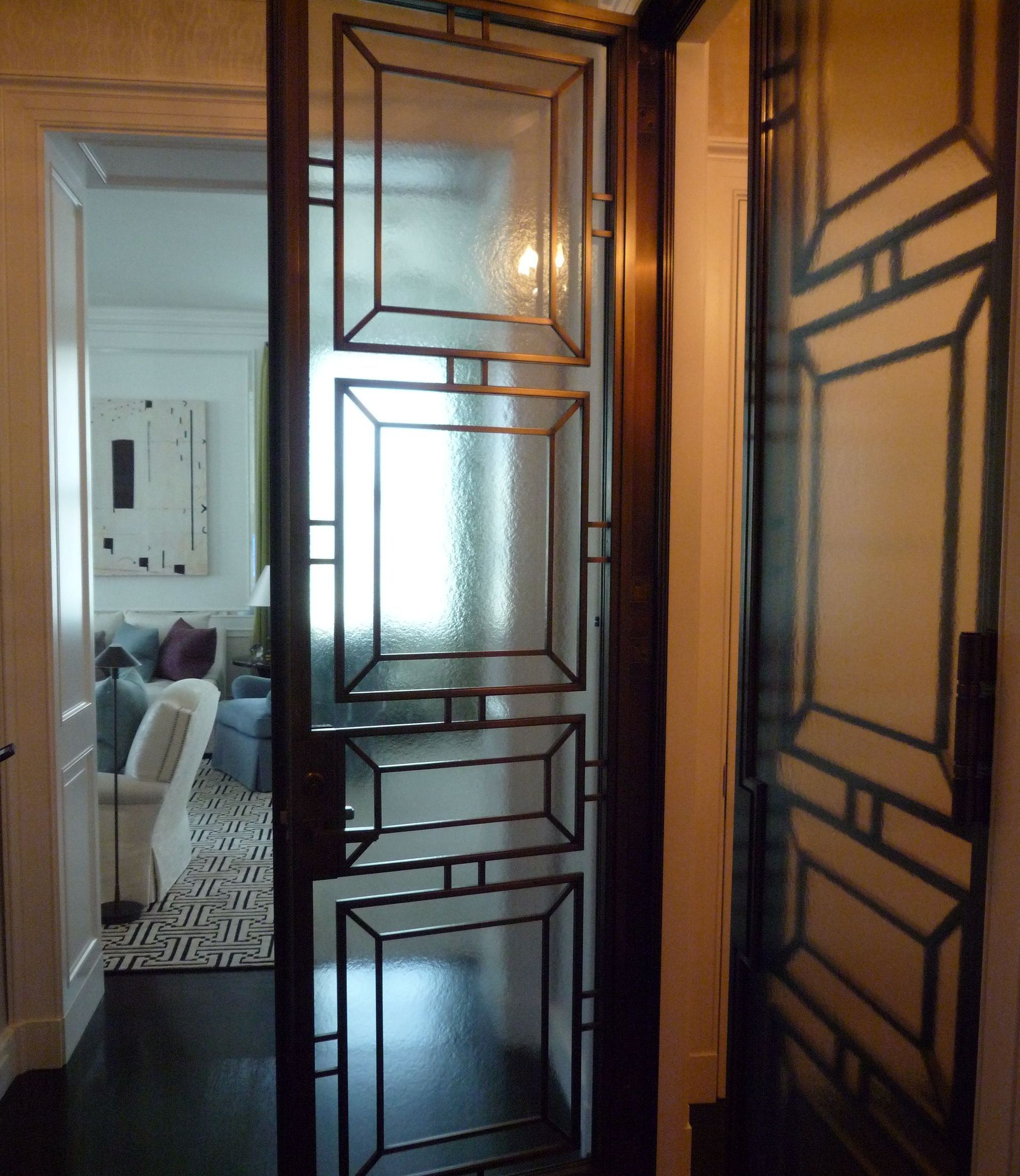 Glass and metal paneled door, open to a living room with a blue couch, art, and white chairs.