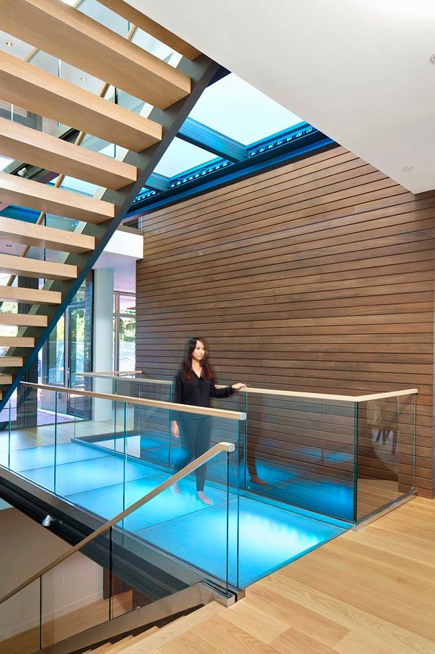 Woman stands on a glass walkway with blue light, wooden stairs and ceiling.