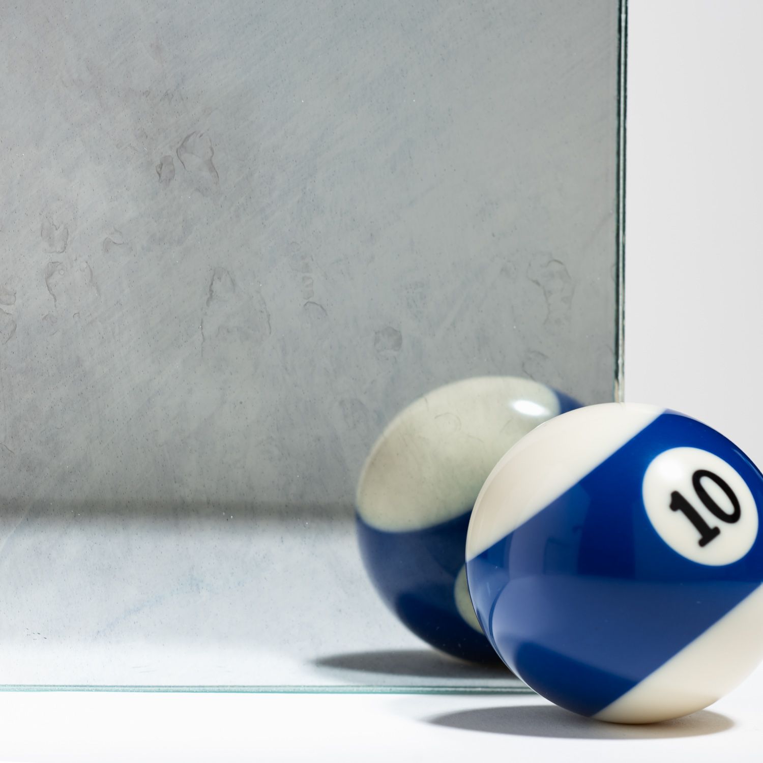 A blue and white number 10 billiard ball sits next to its reflection in a piece of antiqued, distressed mirror glass.