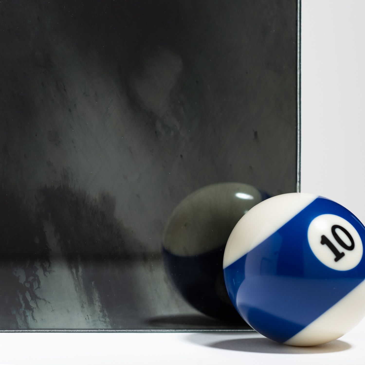 A blue and white number 10 billiard ball sits next to its reflection on a dark, textured, mirrored surface.