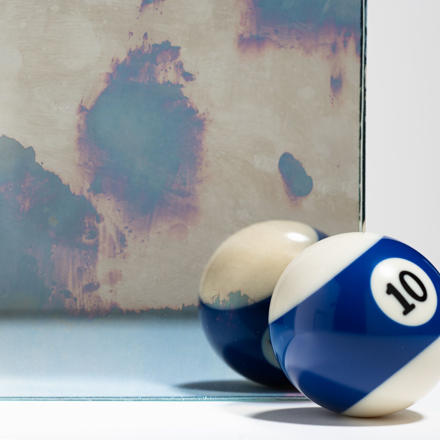A pool ball with the number 10 sits in the foreground, next to another out-of-focus ball before a textured metal backdrop.