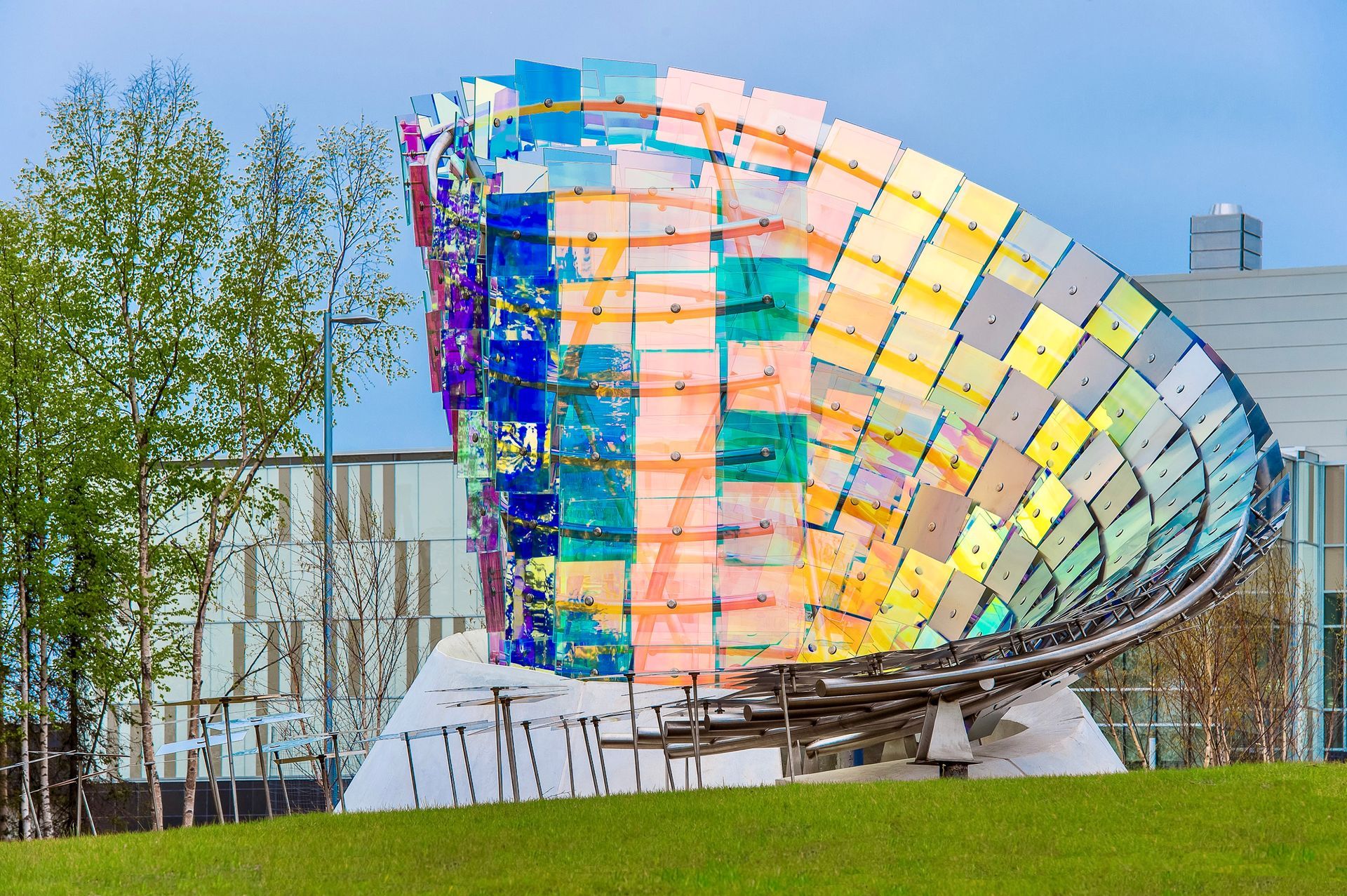 Colorful, abstract sculpture made of glass squares. Located on a grassy knoll in front of a building.