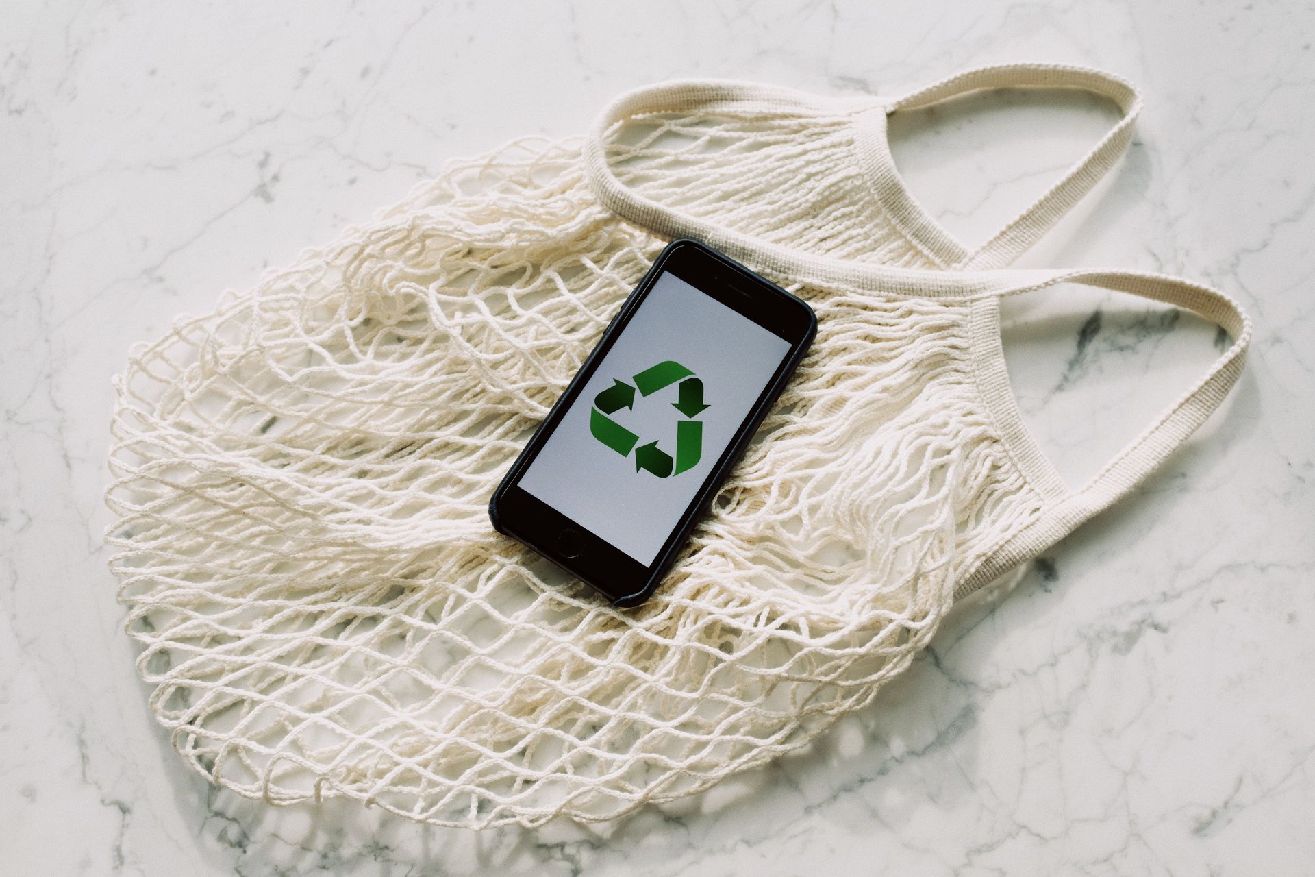 A reusable bag with a phone on top with the recycling symbol.