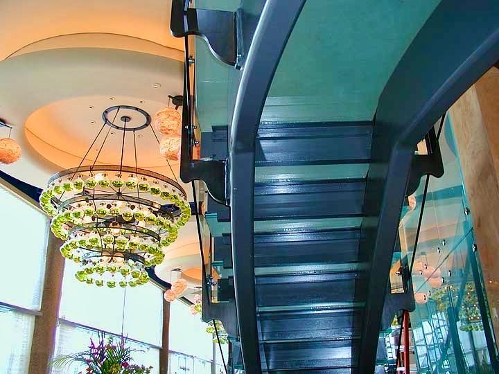 A picture of a glass staircase from below with a green glass chandelier next to it.
