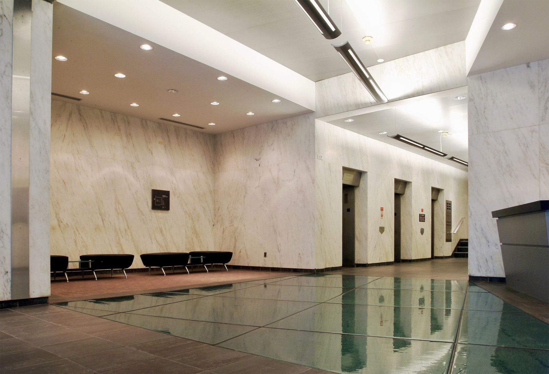 Spacious lobby with marble walls, reflective floor, seating, elevators, and a reception desk.
