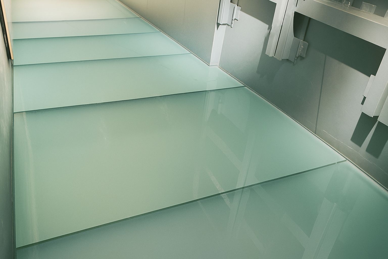 Glass floor hallway with bright lighting, visible supports, and a sleek, modern design.