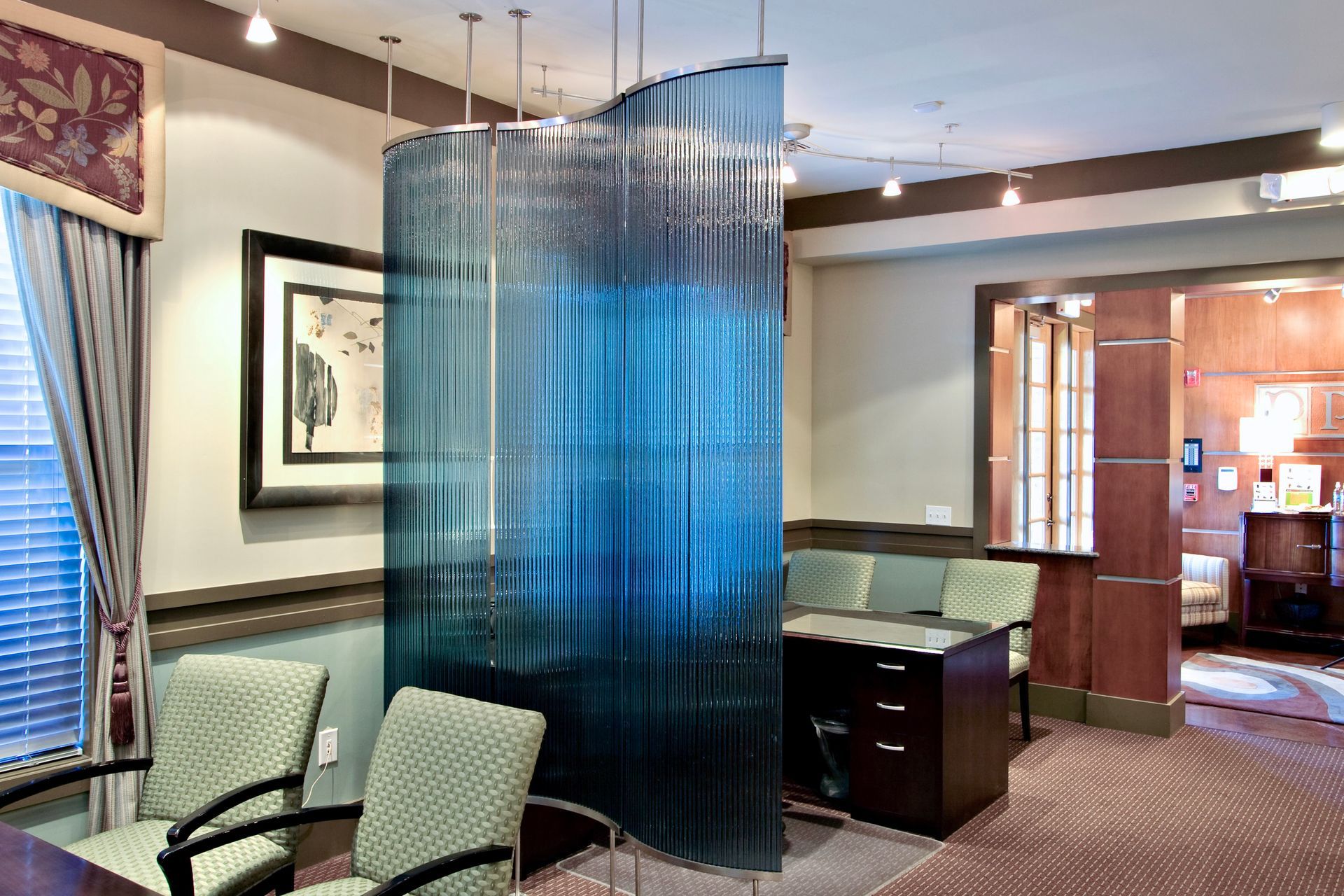 A waiting room with a blue bent and tempered glass between two chairs and a desk