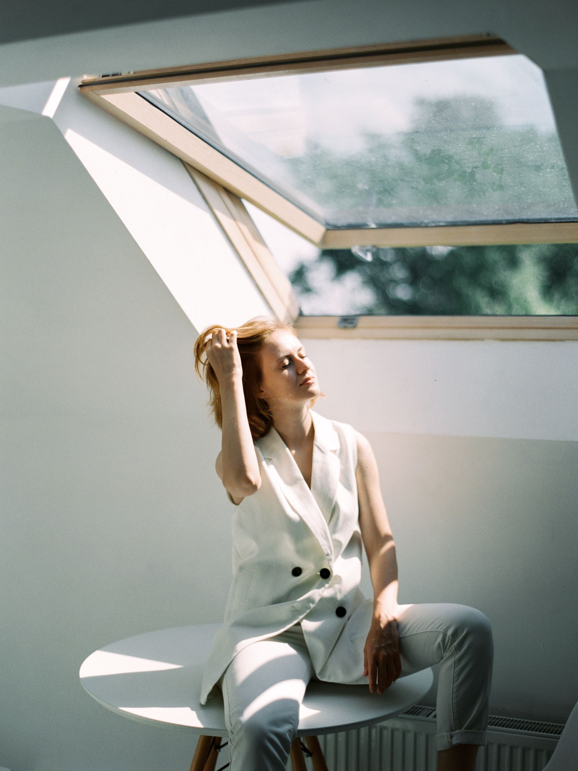 A woman sitting underneath an open window with sunlight pouring in.
