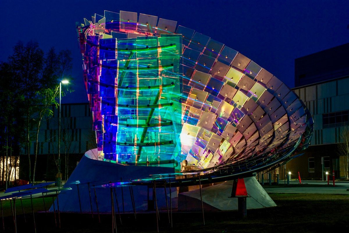 A large sculpture is lit up at night in front of a building.