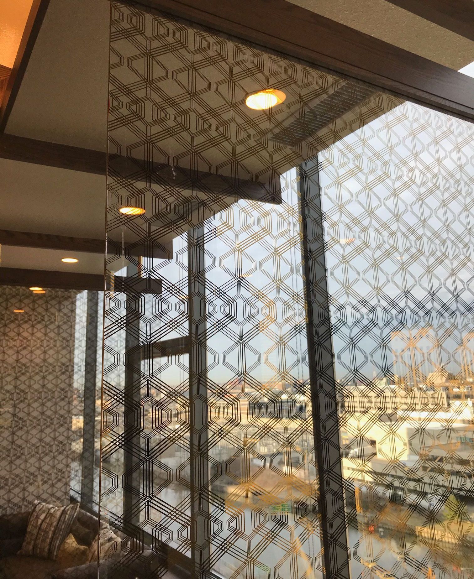 Modern interior with patterned glass walls and city view. Brown trim, gold accents.