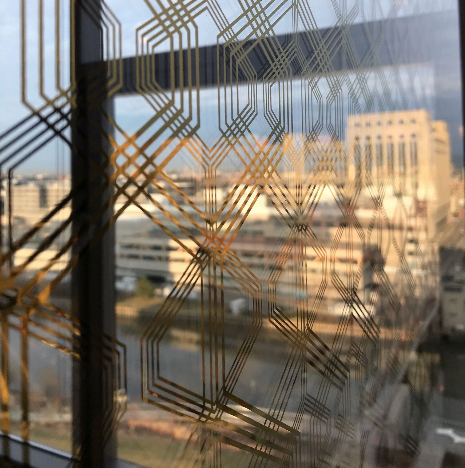Geometric gold pattern on glass window overlooking a city with beige buildings.
