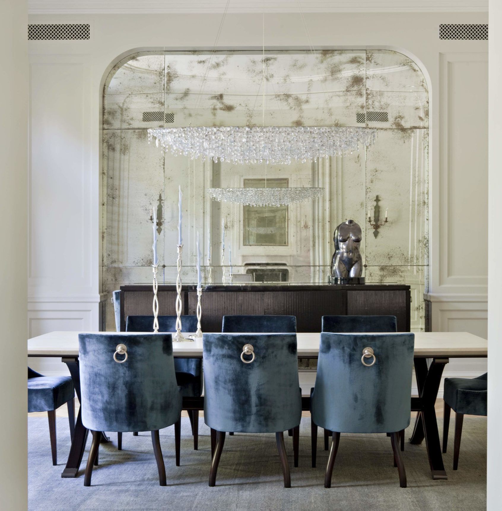 A dining room with blue chairs and a large antique mirror