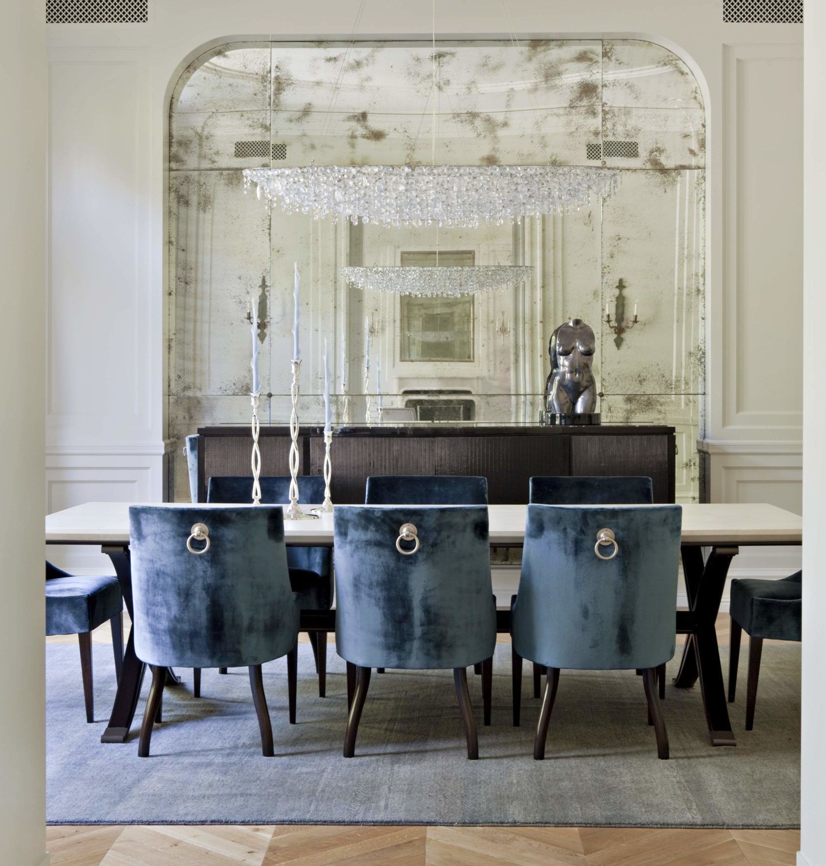 A dining room with blue chairs and a antique mirrored wall