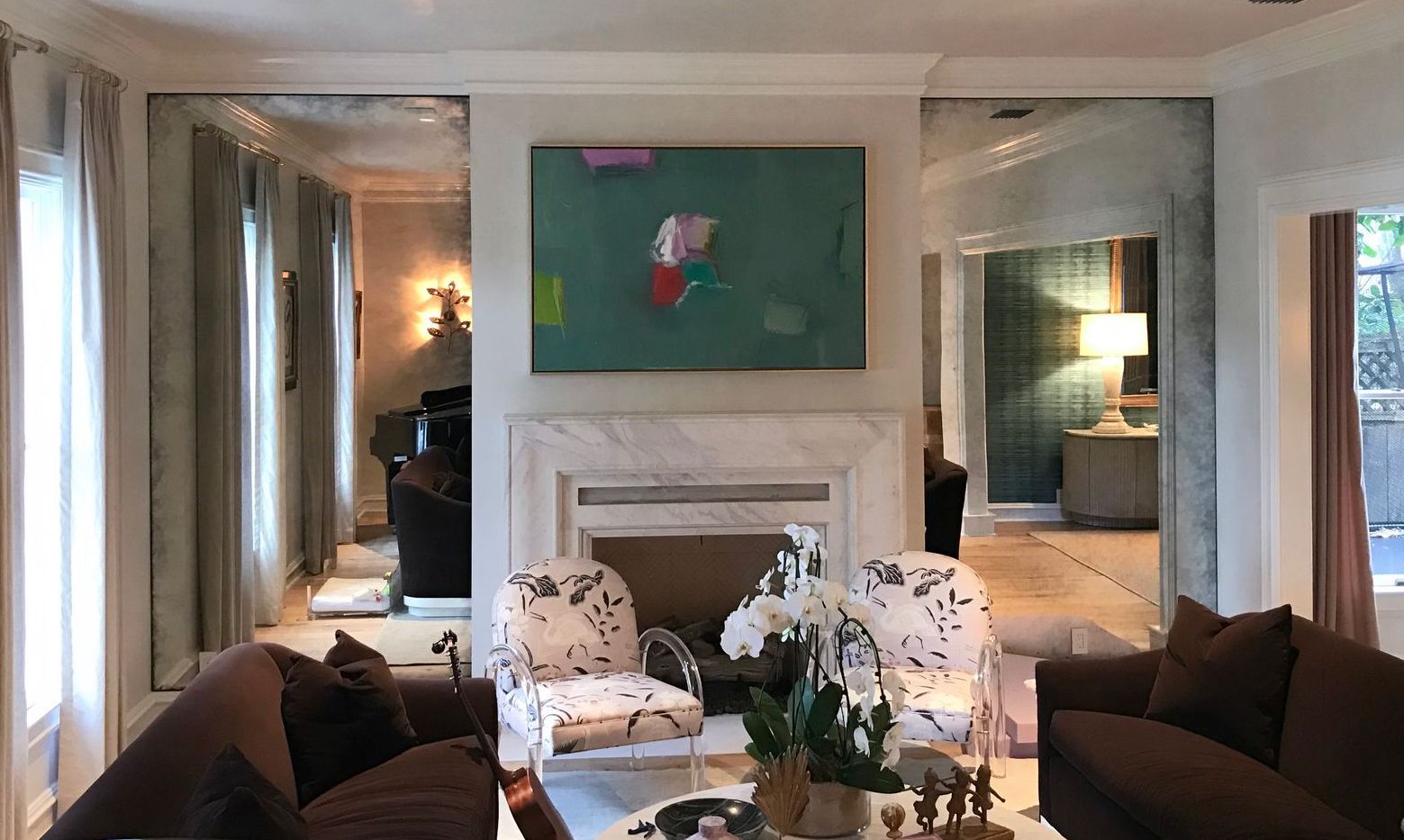 A living room with a fireplace, couch , chairs and a painting on the wall with antique mirrors
