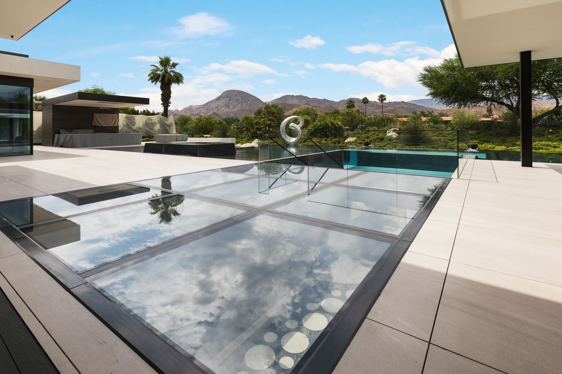 Modern backyard pool with glass water feature, patio tiles, and desert mountains in the background