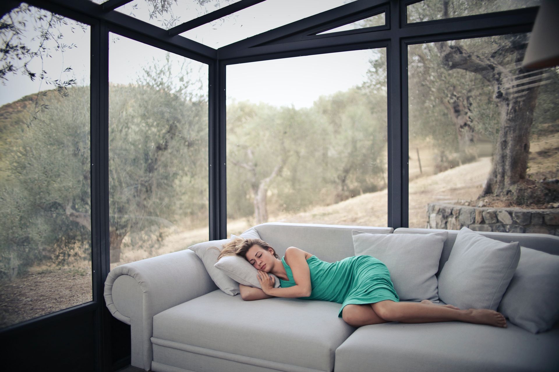 A woman sitting on a couch in a room surrounded by glass walls.