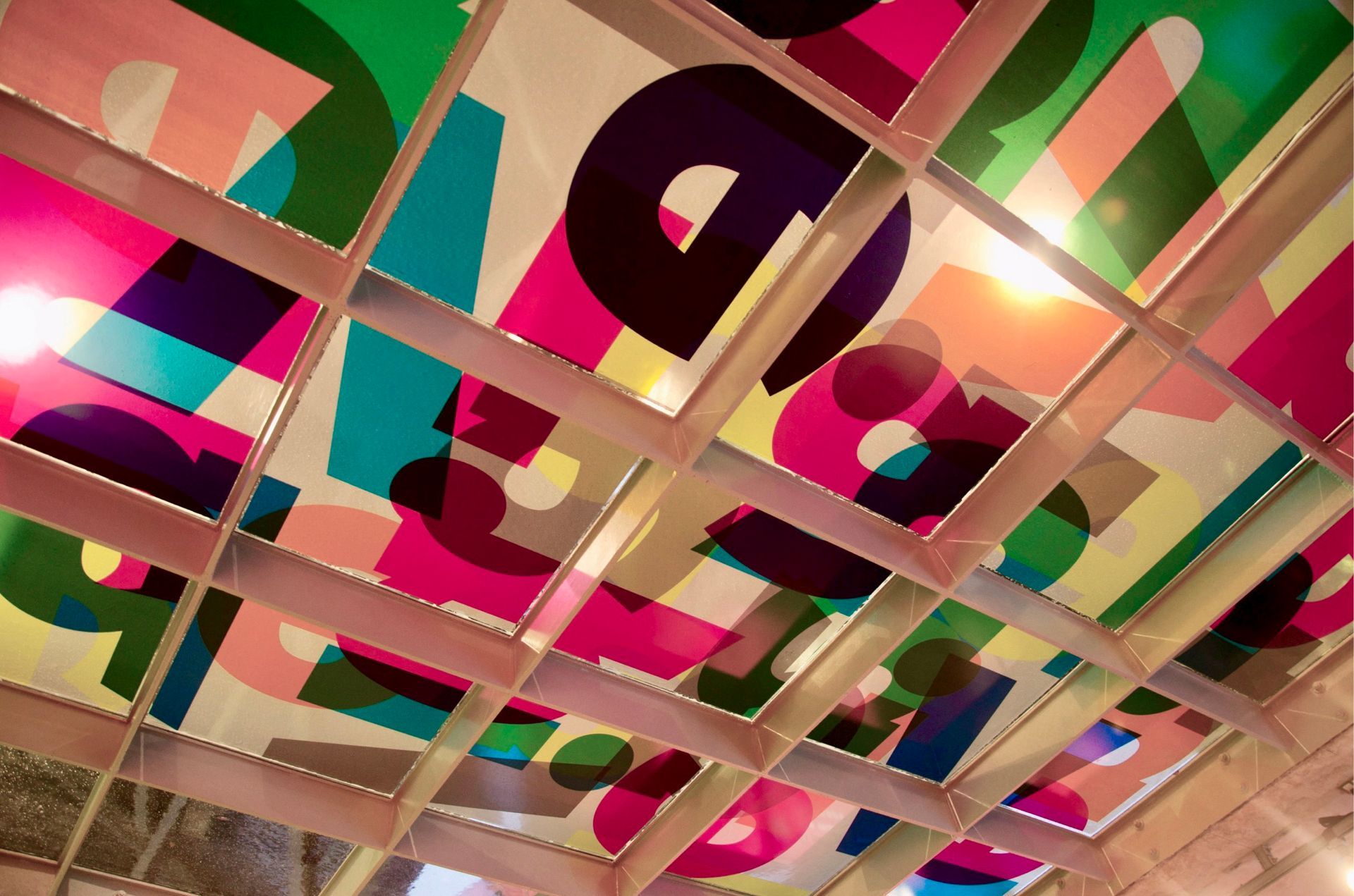A ceiling installation made of square panels featuring colorful, overlapping large-scale letters in various fonts.
