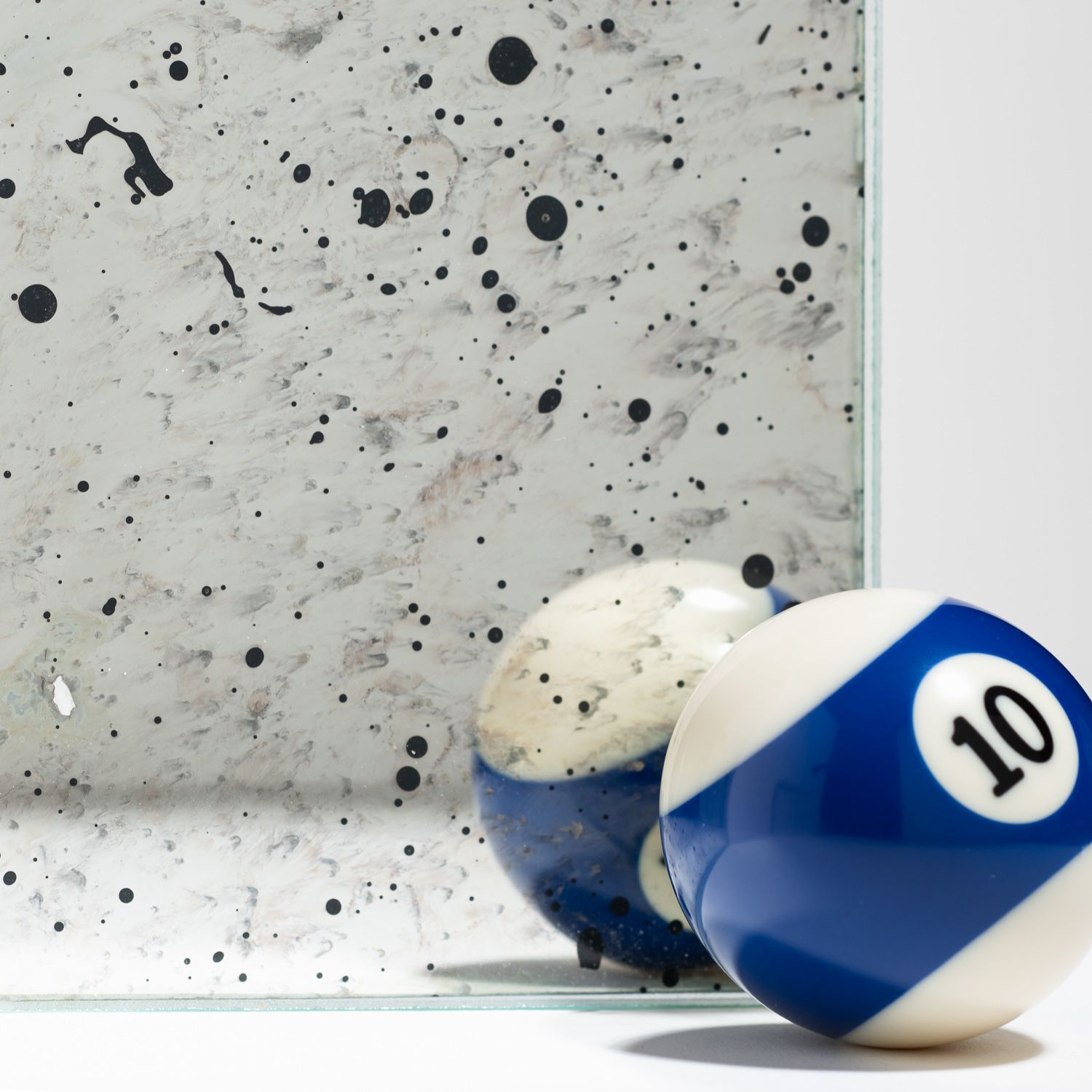 A blue and white number 10 billiard ball sits next to its reflection in a speckled, antiqued mirror.