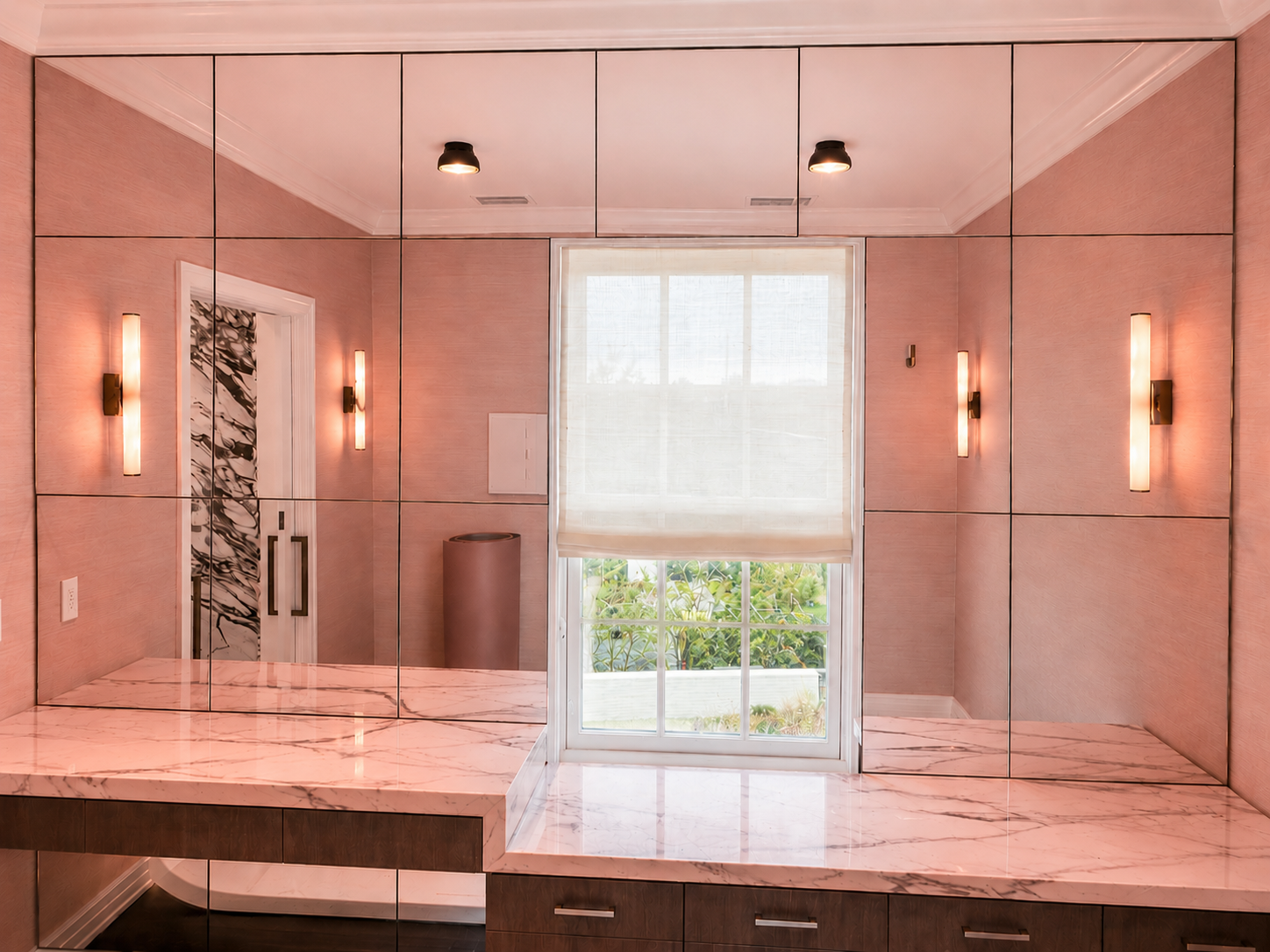 Pink mirror bathroom with glass shower, large window, and wall sconces