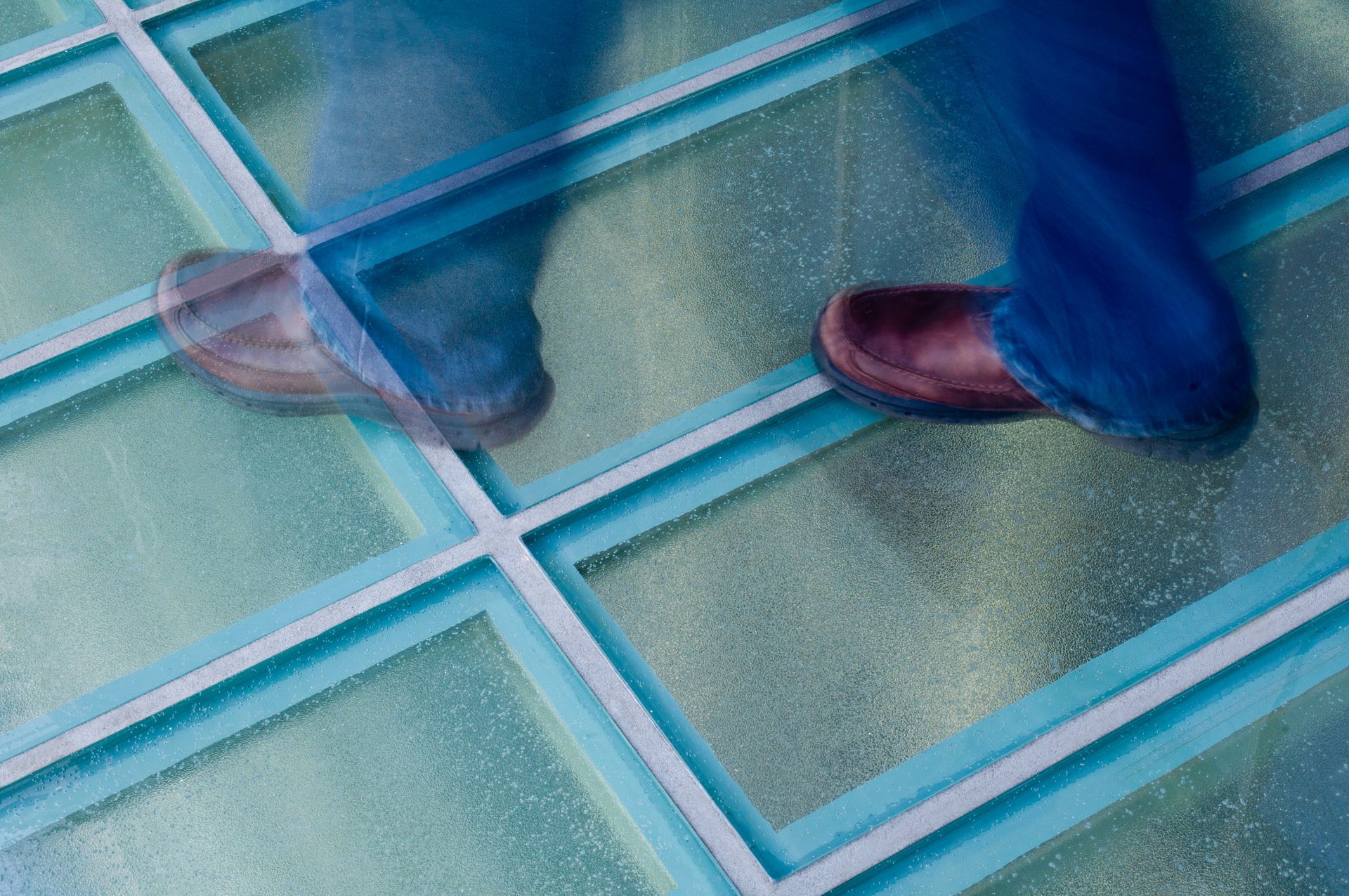 A person walking over glass floor, which is allowing natural light into the level below.