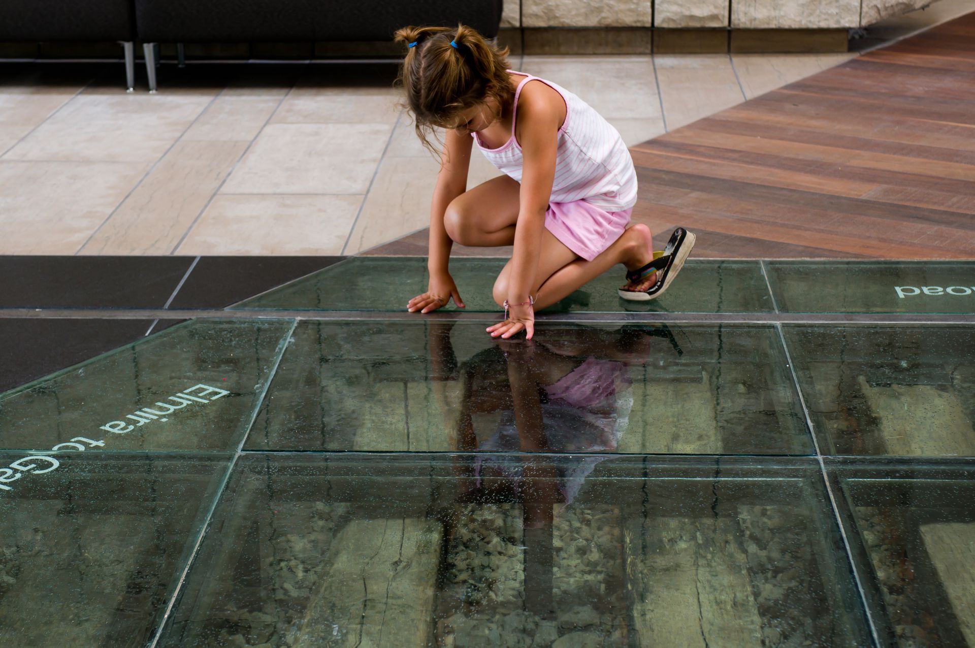 A young girl crouching on transparent glass flooring at a museum.