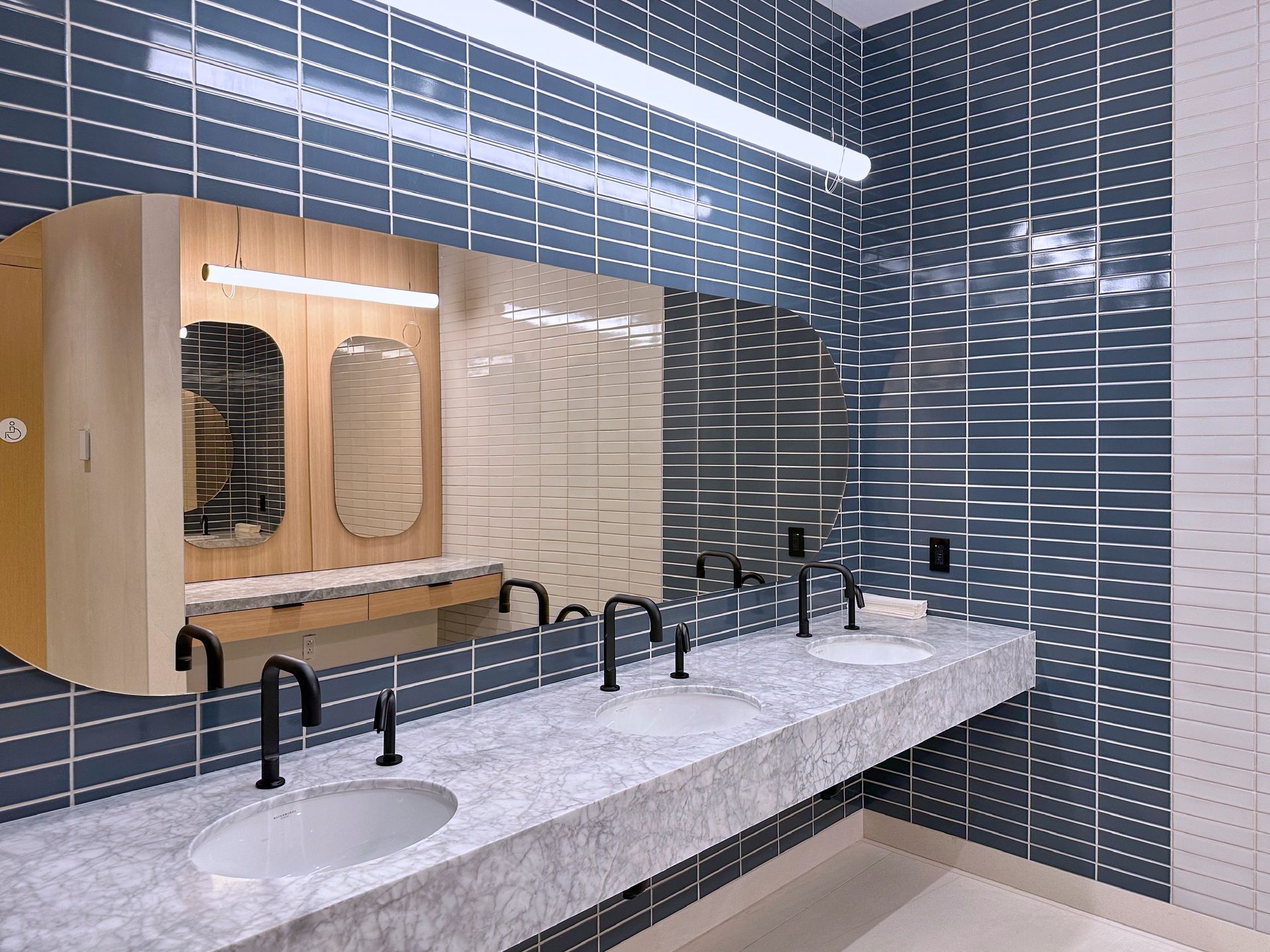 Modern public restroom with gray sinks, black faucets, blue tile walls, and large champagne color mirrors.