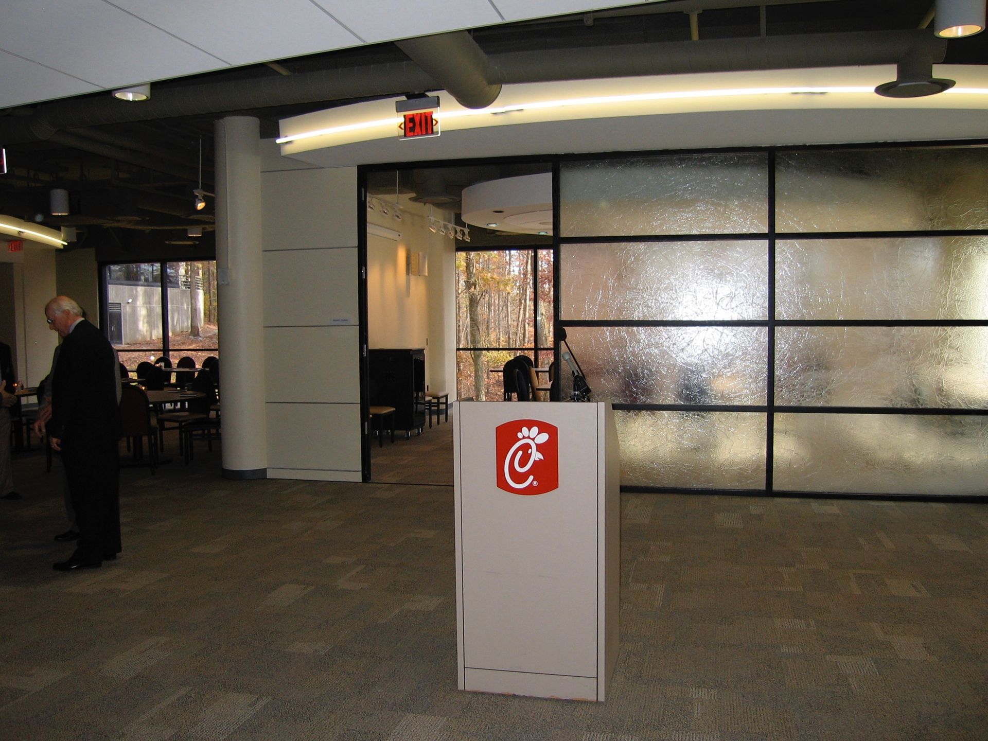 Chick-fil-A podium in a room with a frosted glass wall. A man in a suit stands nearby.