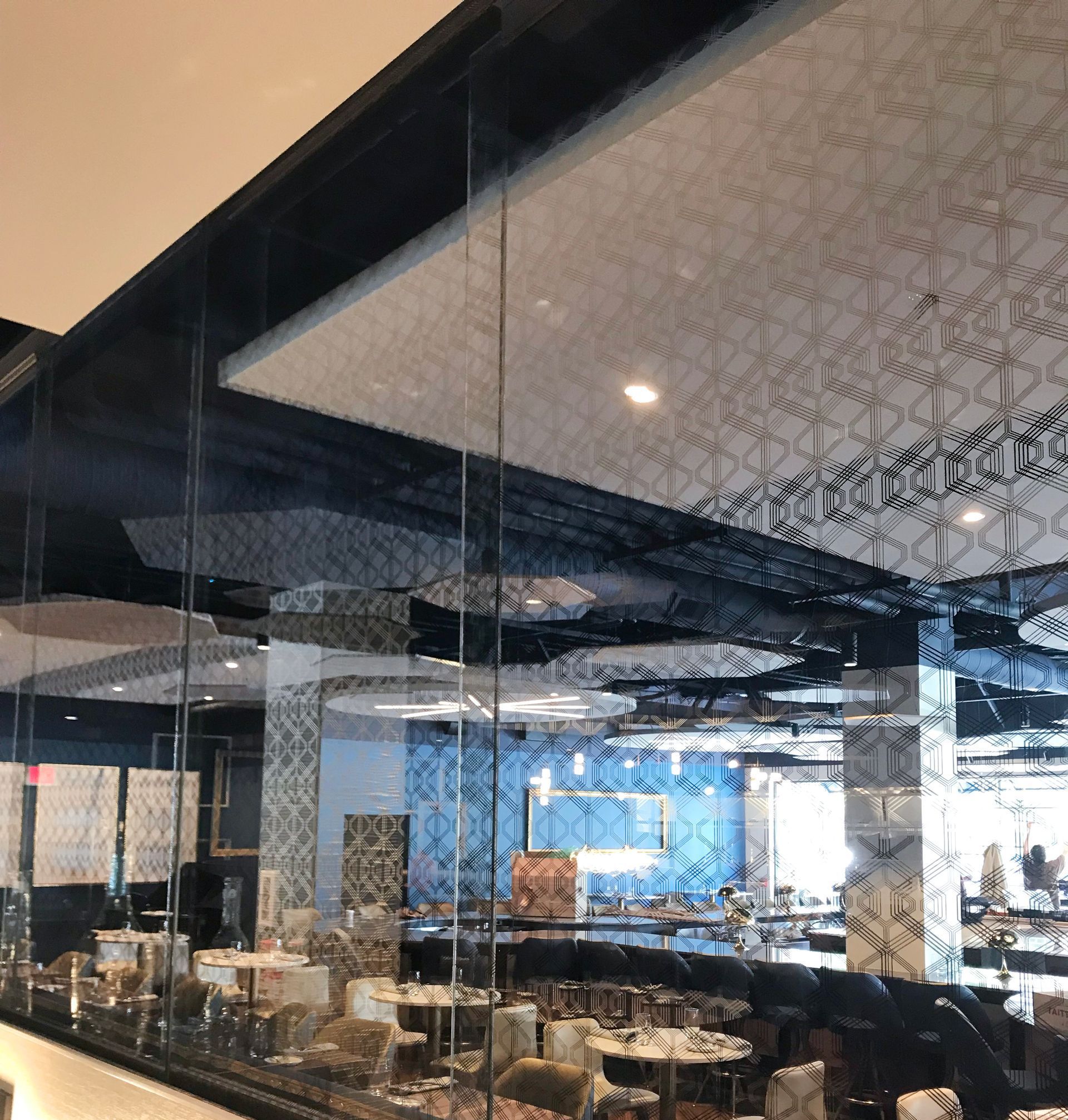 Restaurant interior with glass walls, tables, and patterned ceiling. Blue tile accents visible.
