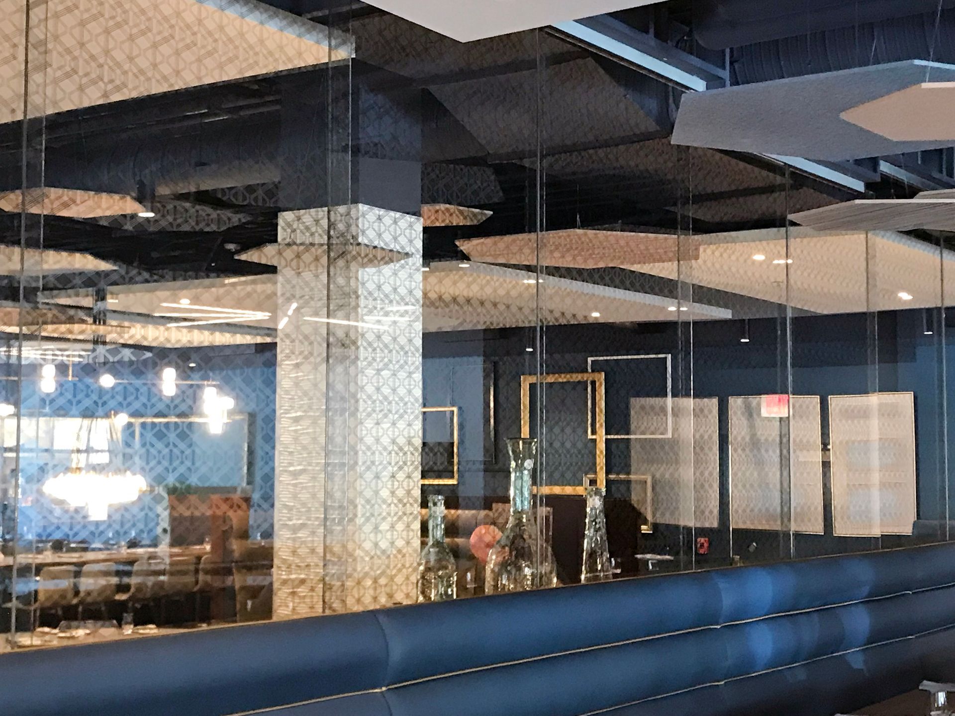 Interior restaurant scene with reflective surfaces, patterned ceiling tiles, and blue booth seating.