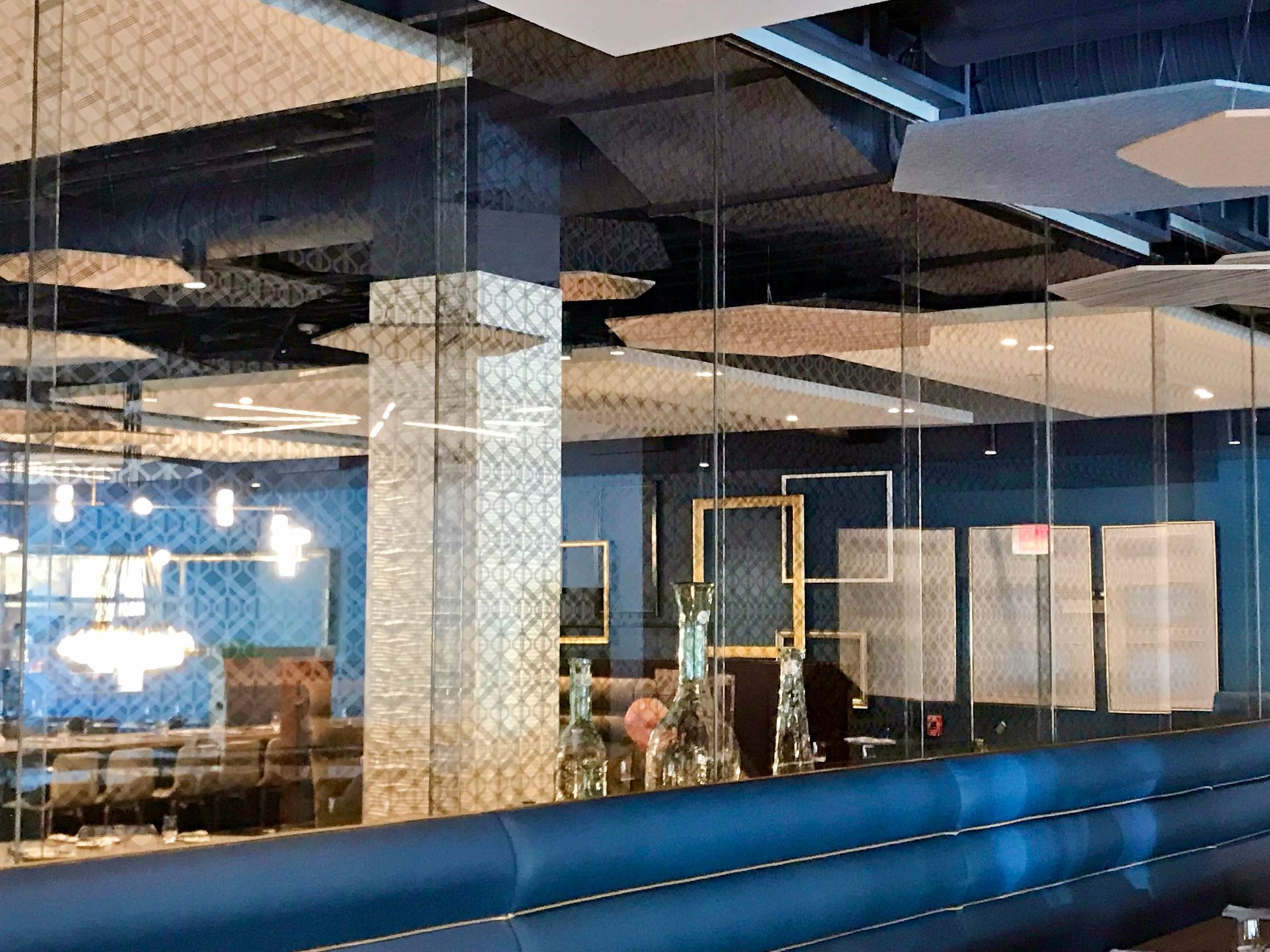 Restaurant interior with blue booths, mirrored columns, and patterned ceiling panels.