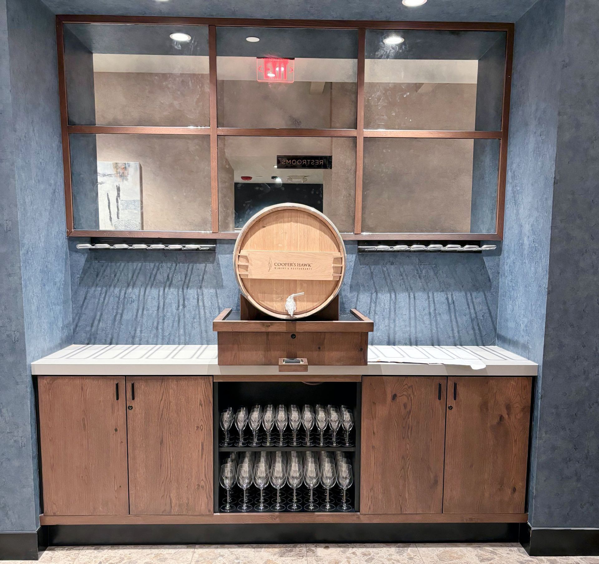 A wooden barrel sits on top of a counter next to a antique mirror shelf of wine glasses.