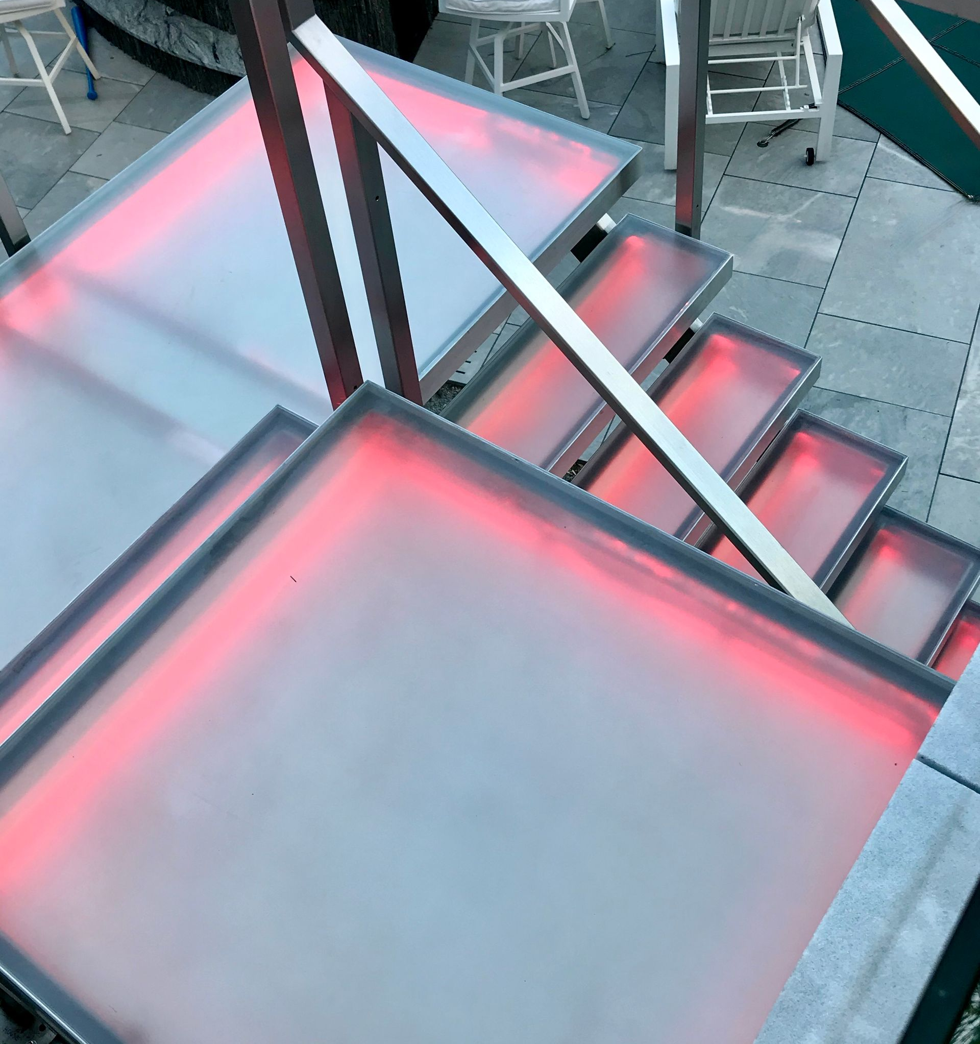 Modern outdoor staircase with semi-transparent steps backlit by glowing red LED lights, viewed from above.