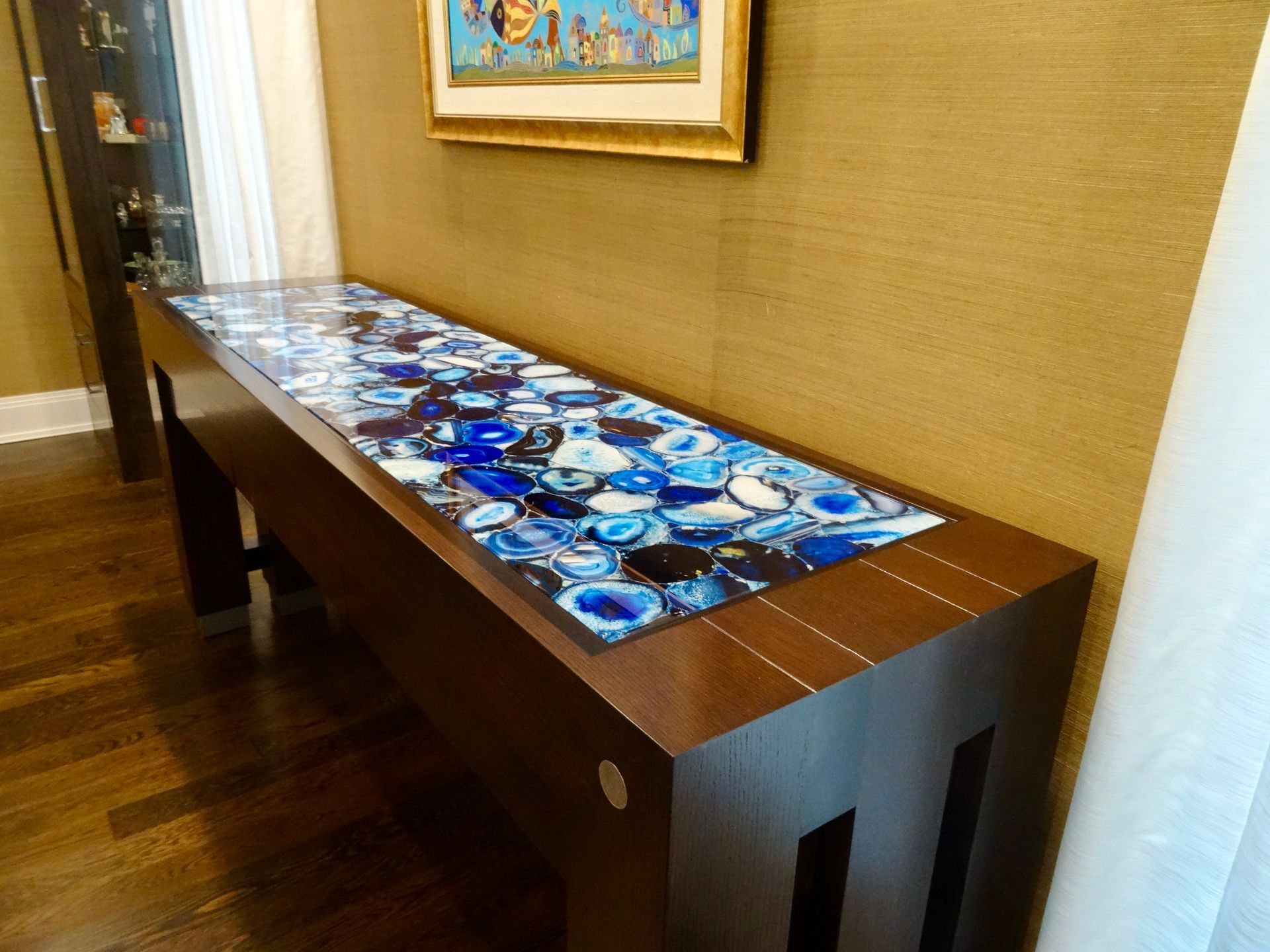 Long wooden console table with blue agate stone top in room with art and wood floor.