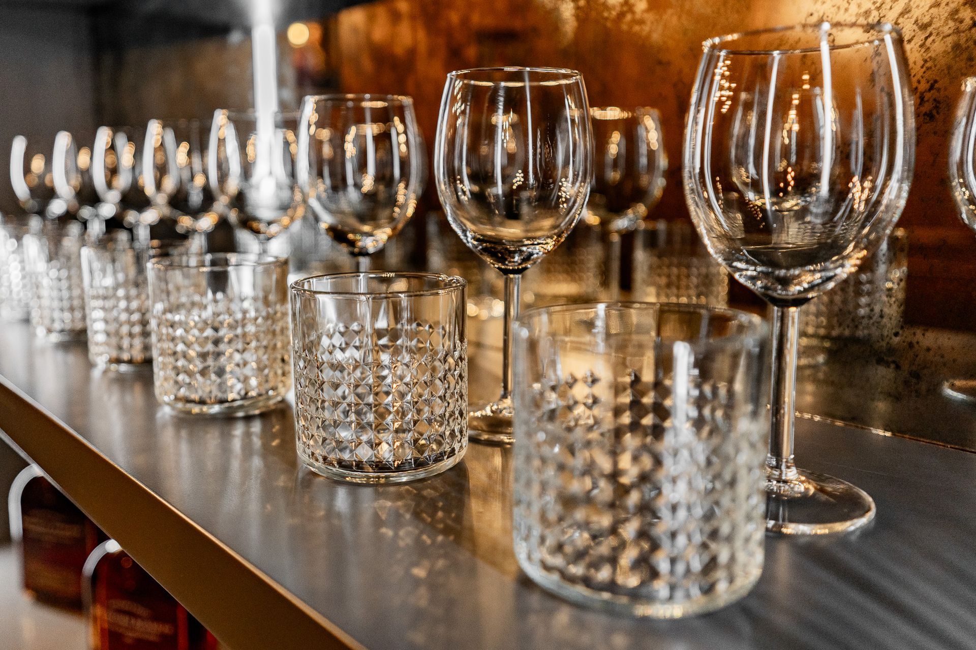 A row of wine glasses and glasses on a bar.