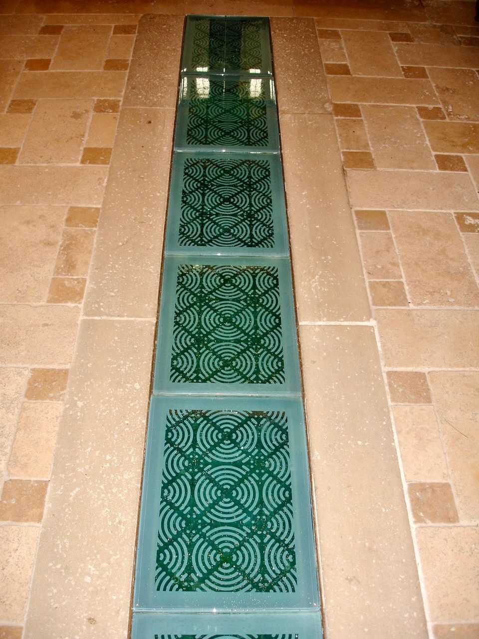 Green patterned glass flooring set in a floor surrounded by beige stone tiles.