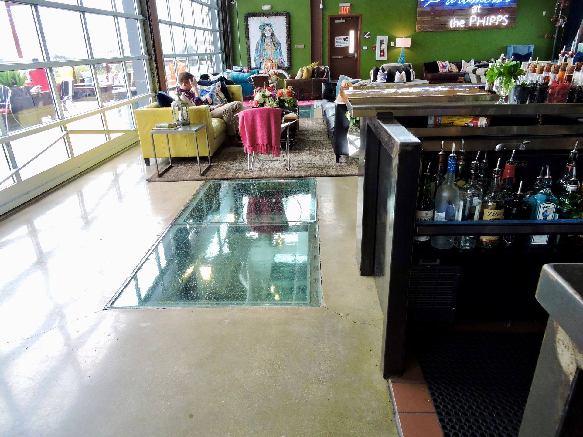 Interior of a bar with a glass-floored section revealing a lower level. People sit on couches.