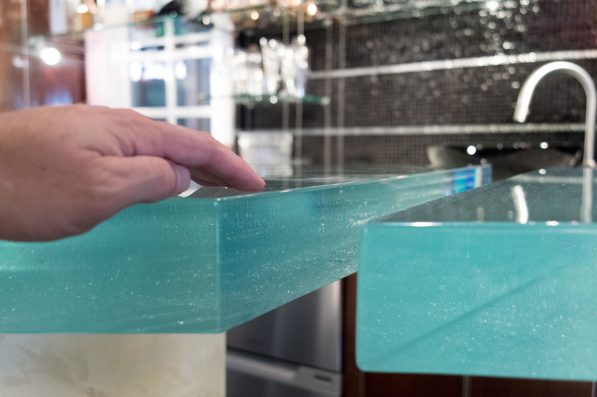 A hand resting on a custom thick glass countertop.