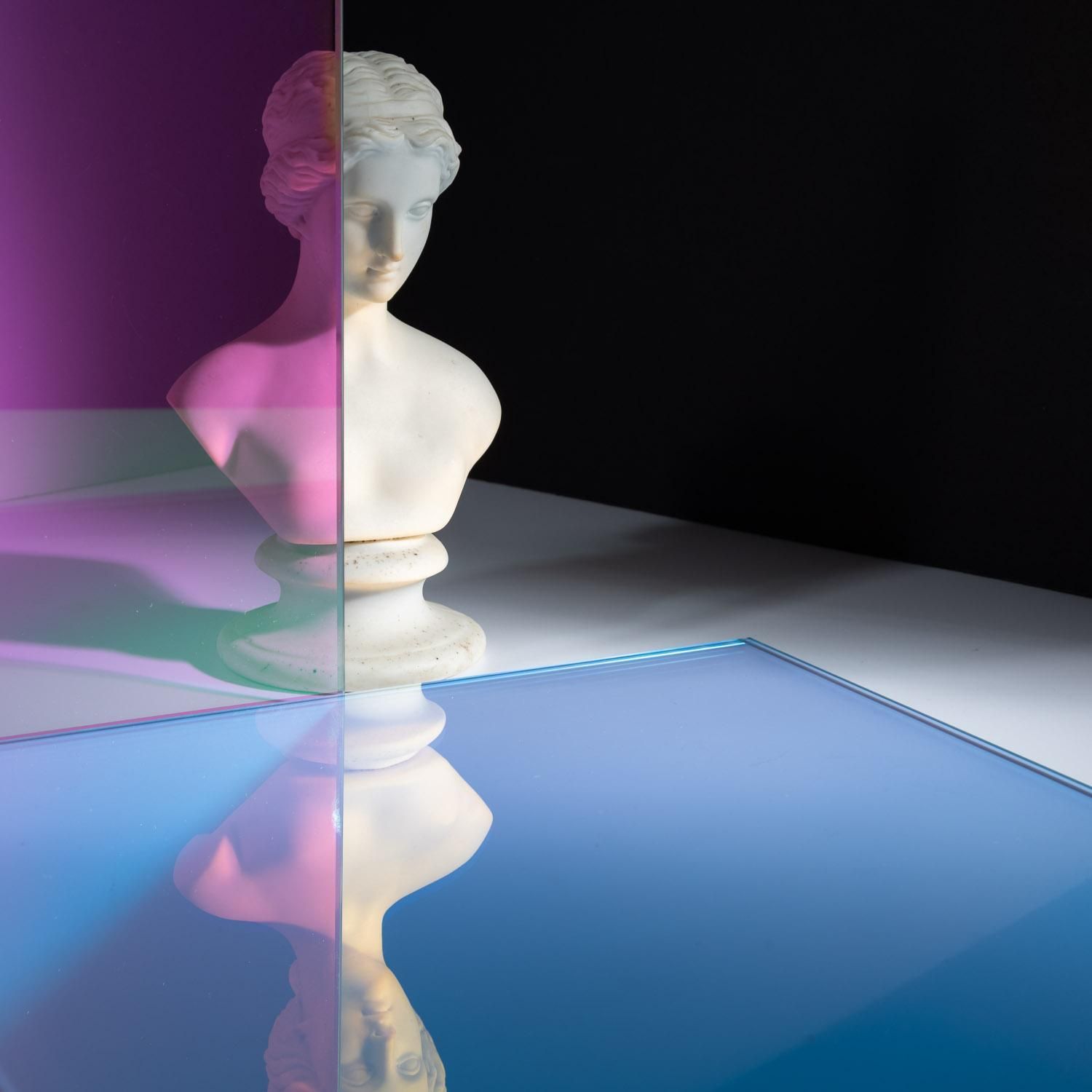 A white bust reflecting onto a piece of dichroic glass that's showing as purple and blue.