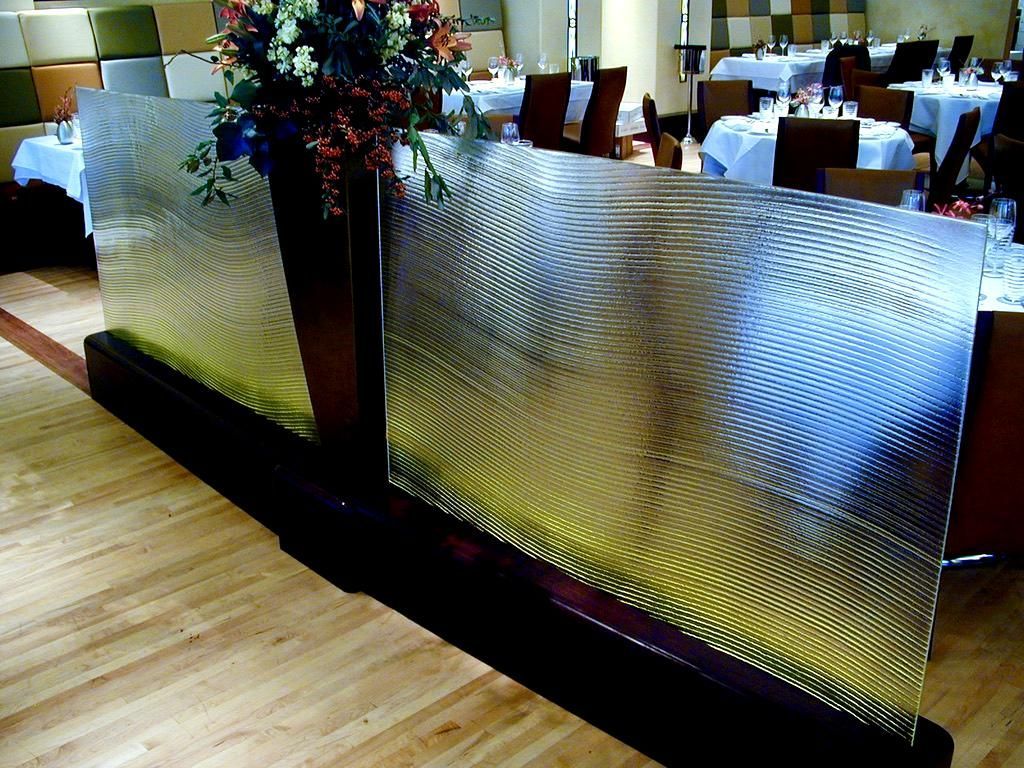 Decorative glass panel in a restaurant, with floral arrangement. Wooden floor and tables in background.