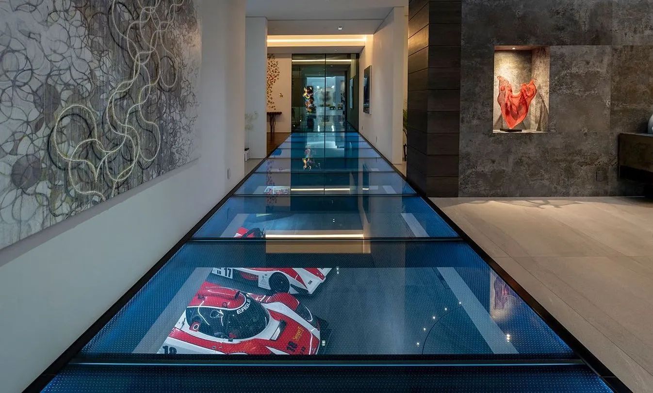 Long hallway with a glass floor displaying a sneaker collection; art on walls.