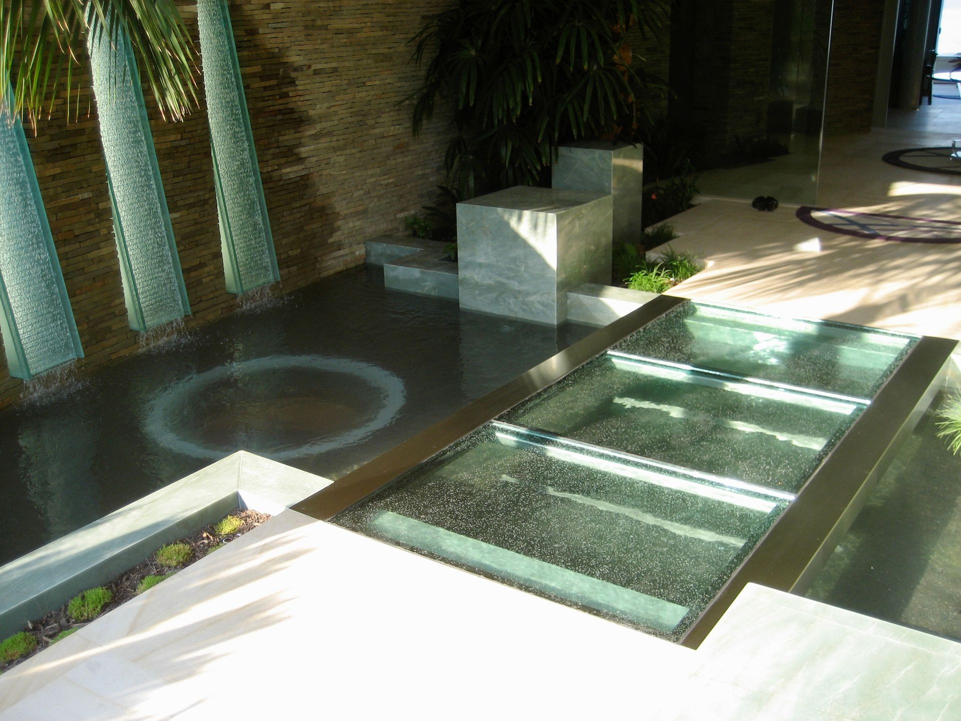 A modern outdoor water feature with stone pillars, a reflecting pool, and a rectangular glass floor.