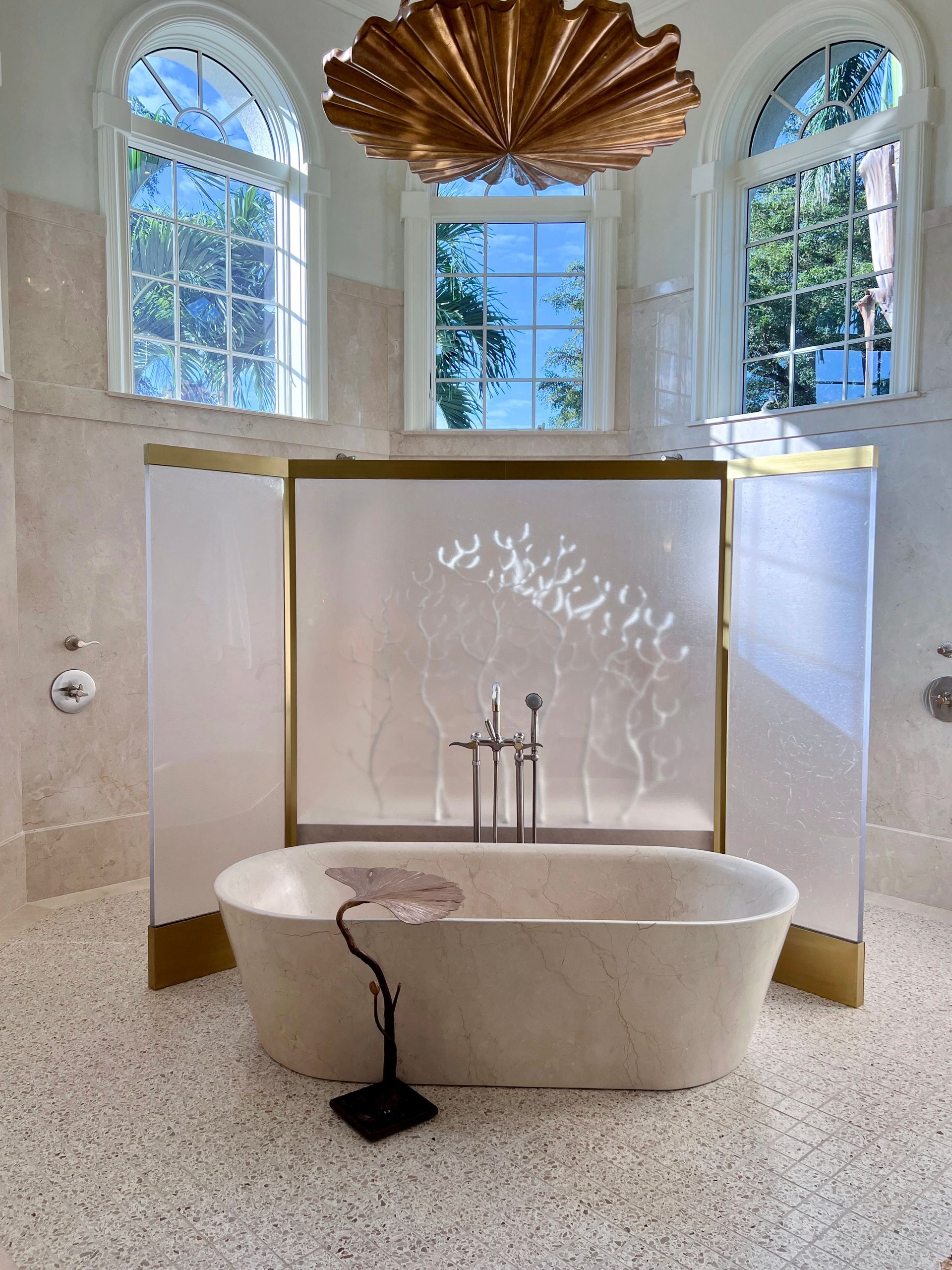 Luxurious bathroom with freestanding tub, ornate gold light fixture, arched windows.