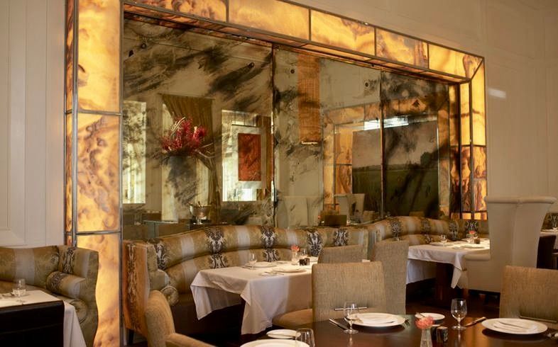 A restaurant with tables and chairs and a large antique mirror on the wall.