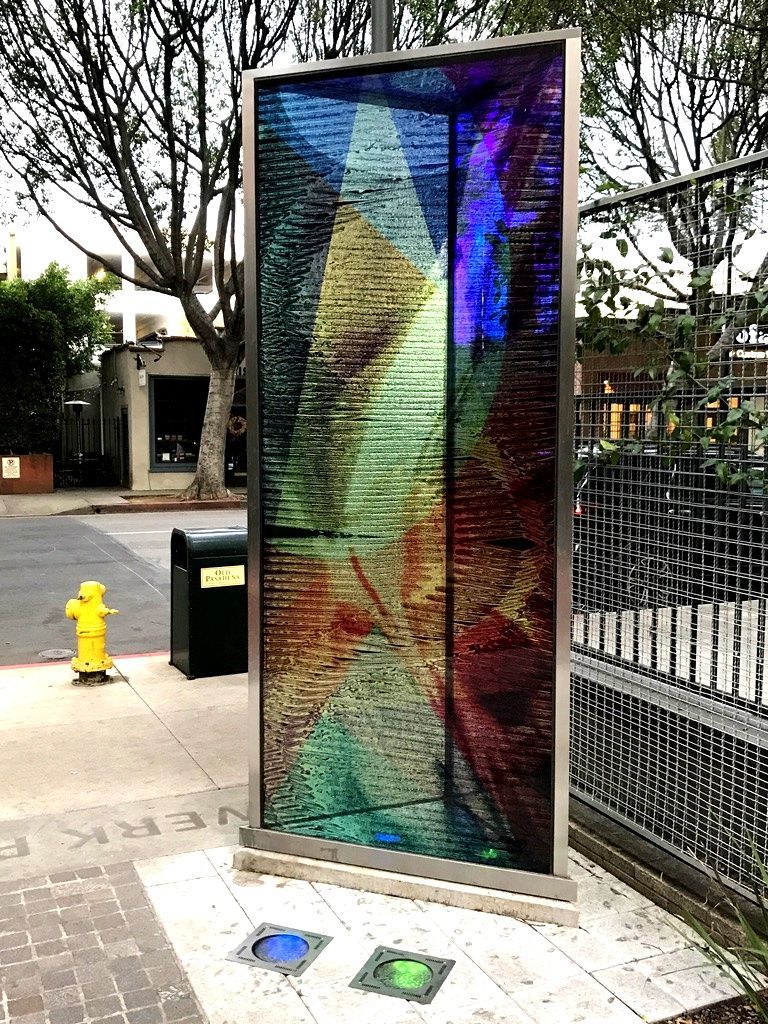 Colorful outdoor art glass installation with light effects, framed in metal. Two ground lights in front.