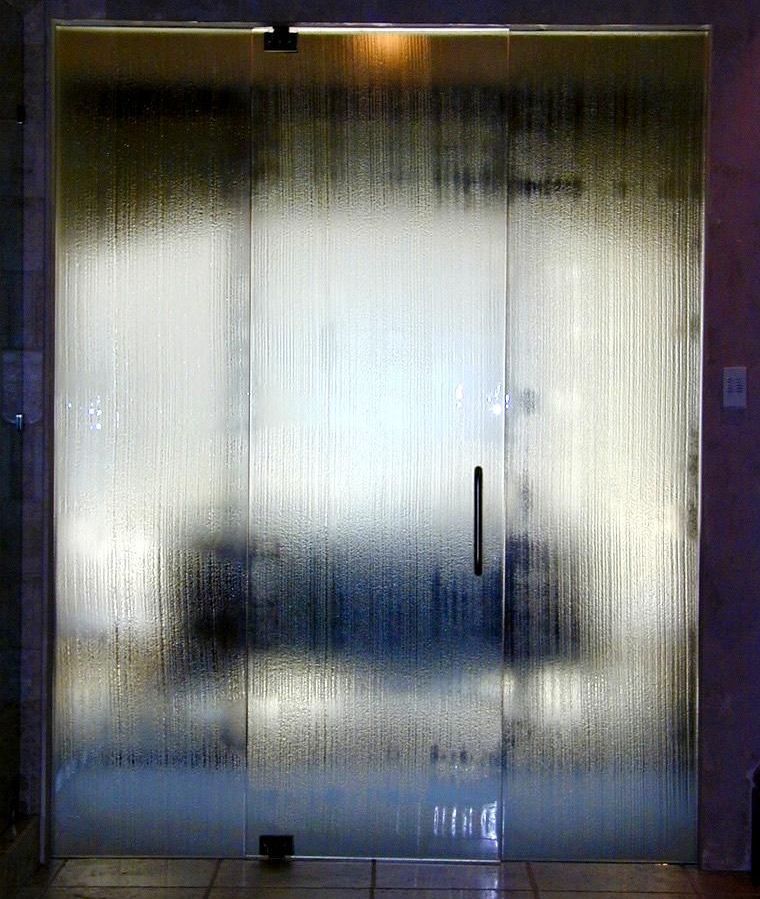 Steamy glass shower doors with vertical streaks, obscuring the interior. Black handle, tile floor.