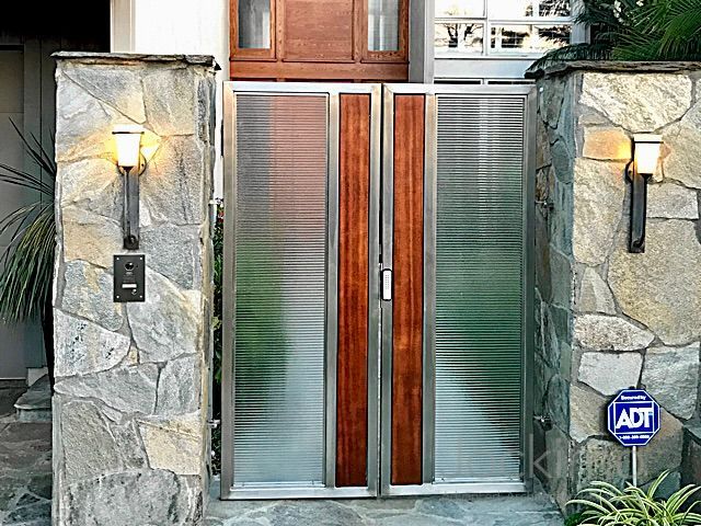 A modern double gate made of fluted cast glass and wood between two stone pillars.